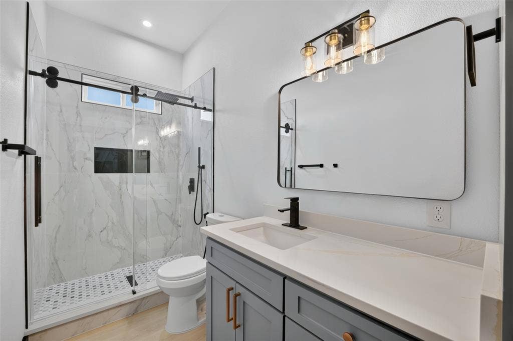 601 Melody Circle, Kaufman, TX 75142 Gray cabinetry with matte hardware, stone-composite countertop, glass-enclosed walk-in shower with stone-tile surround, and rectangular wall-mounted mirror