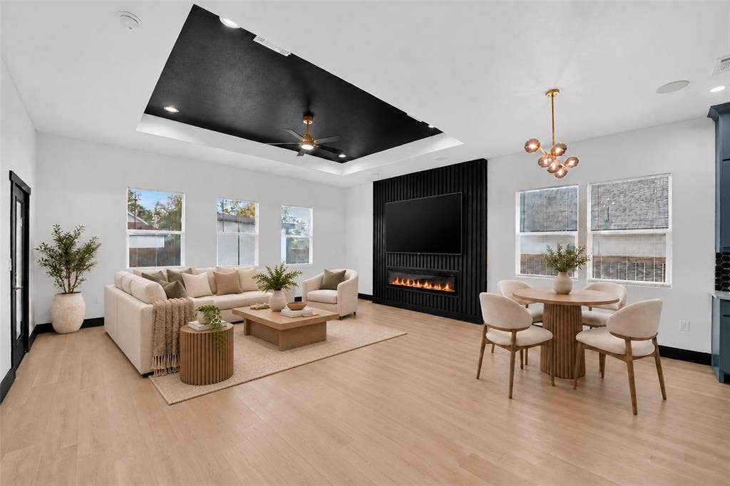 601 Melody Circle, Kaufman, TX 75142 Open-concept area featuring a black recessed tray ceiling with an integrated ceiling fan, light wood-finish flooring, and a vertical-slat accent wall with a built-in linear electric fireplace