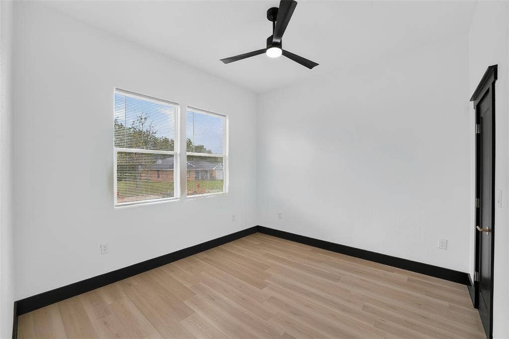 601 Melody Circle, Kaufman, TX 75142 Neutral-toned room featuring wood-finish flooring, matte black trim, a minimalist ceiling fan with integrated lighting, and dual windows