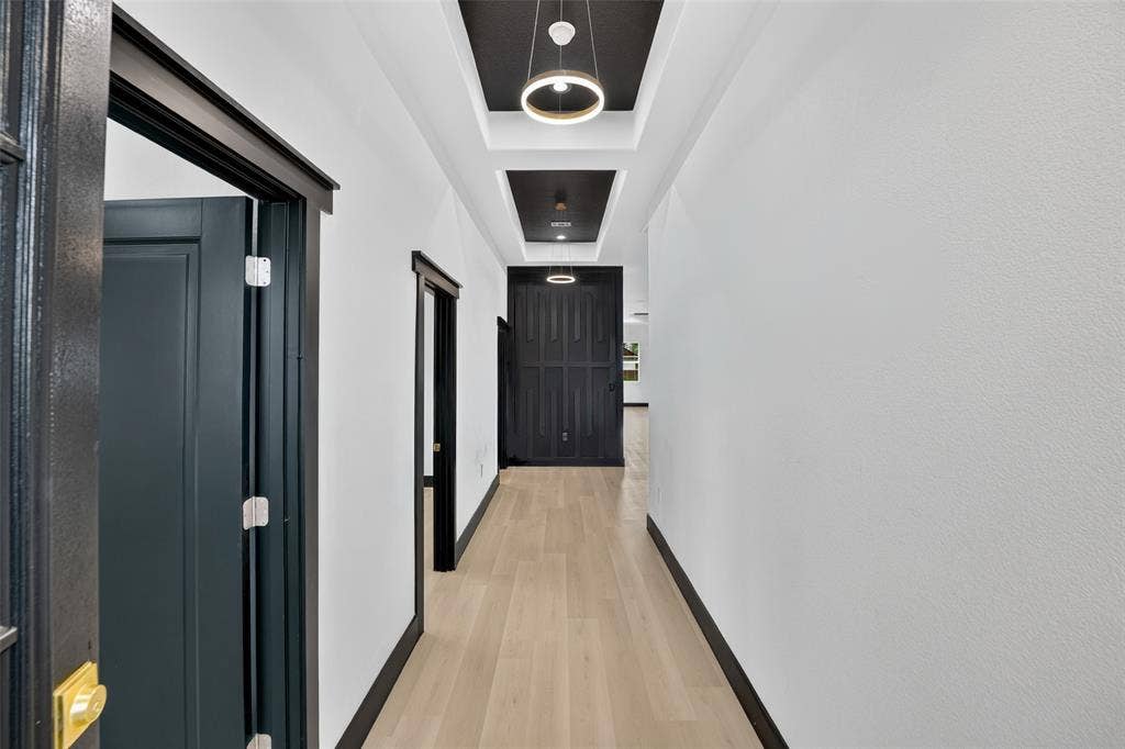 601 Melody Circle, Kaufman, TX 75142 Hallway featuring wood-finish flooring, recessed tray ceilings with dark-toned architectural accents, contemporary circular pendant lighting, and high-contrast black interior door frames and trim