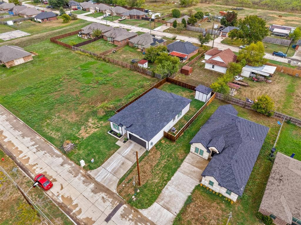 601 Melody Circle, Kaufman, TX 75142 Aerial perspective of a detached single-story residence featuring an asphalt shingle roof, concrete driveway, attached garage, and a fenced yard with a detached storage structure