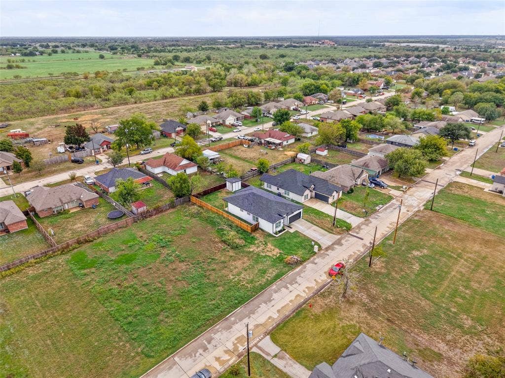 601 Melody Circle, Kaufman, TX 75142 Aerial perspective of a residential lot featuring a single-story structure with a dark shingle roof, paved driveway, enclosed rear yard, and proximity to open green space