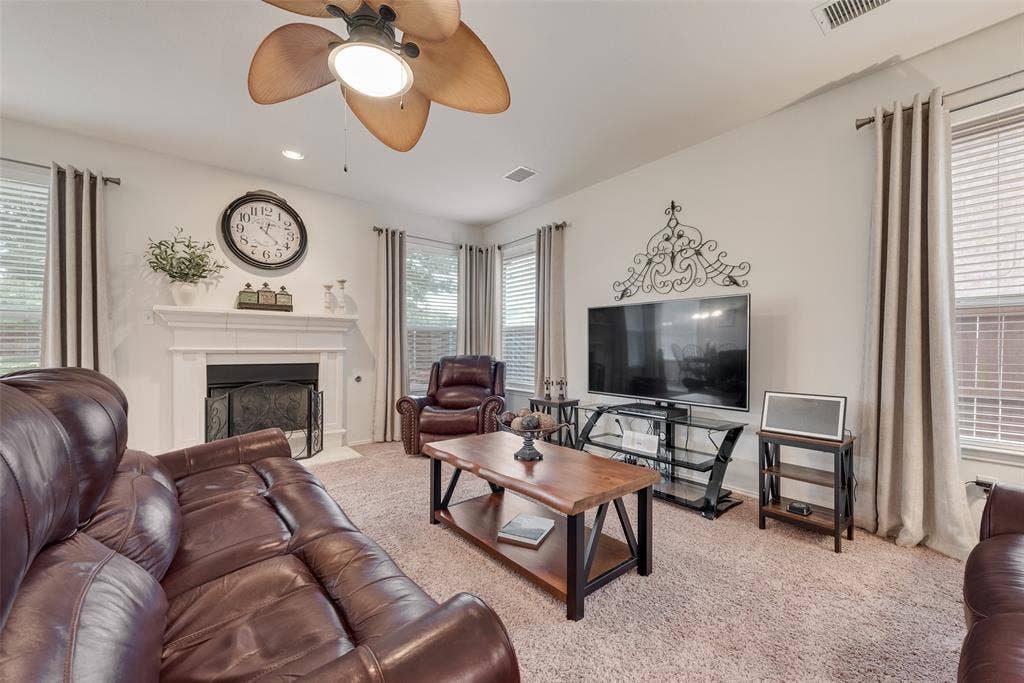 148 Oakbluff Drive, Murphy, TX 75094 Living area featuring a fireplace with a white mantel, high ceilings, multiple windows with neutral drapery, and a multi-blade ceiling fan