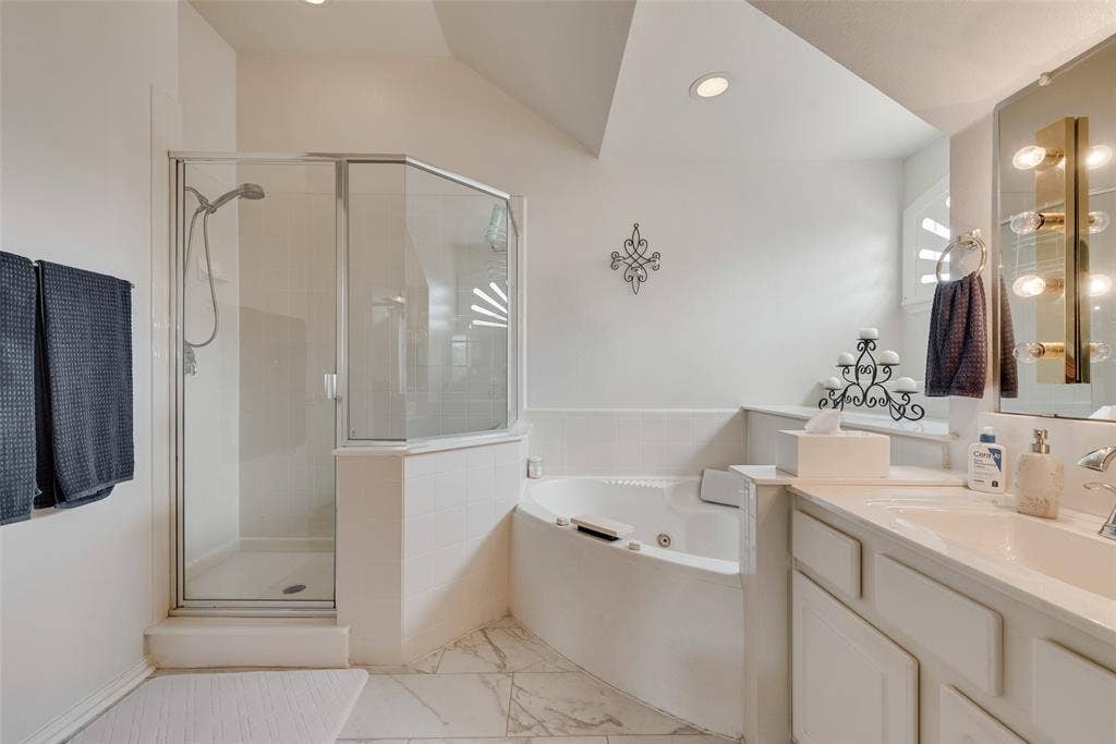 148 Oakbluff Drive, Murphy, TX 75094 Corner soaking tub with tile surround, glass-enclosed shower, built-in vanity with integrated sink, and wall-mounted vanity lighting