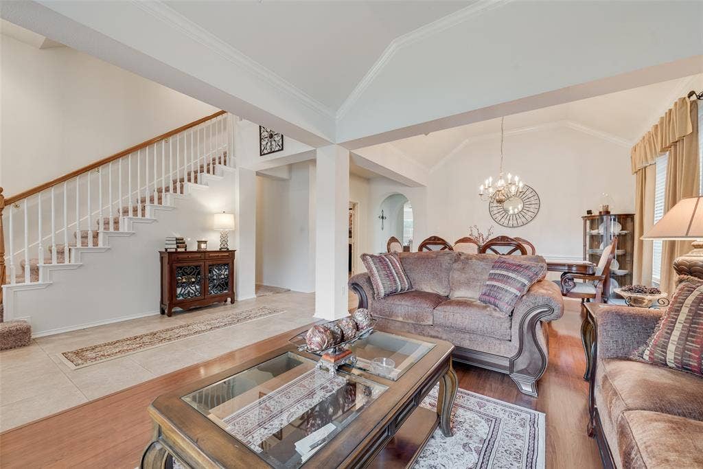 148 Oakbluff Drive, Murphy, TX 75094 Open-concept main level featuring vaulted ceilings, a central staircase with wood handrails, large-format tile flooring, and wood-finish flooring