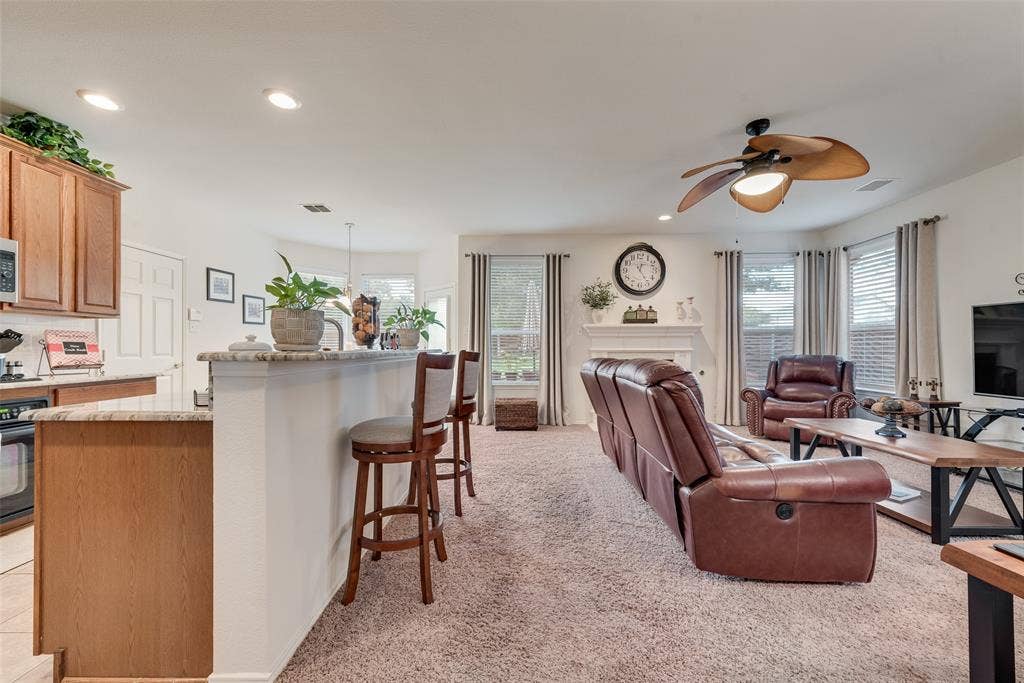 148 Oakbluff Drive, Murphy, TX 75094 Open-concept interior featuring wood cabinetry, stone-surfaced kitchen island, tile-surround fireplace, and decorative ceiling fan with integrated lighting