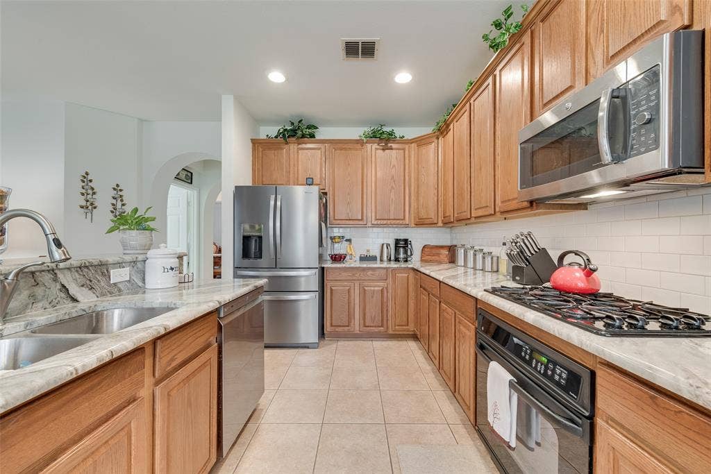 148 Oakbluff Drive, Murphy, TX 75094 Galley kitchen featuring warm wood cabinetry, stainless steel appliances including a French-door refrigerator and gas cooktop, white subway tile backsplash, and quartz countertops with an undermount sink