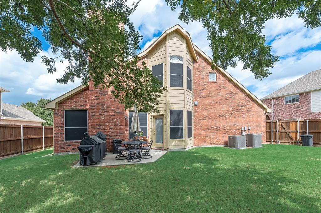 148 Oakbluff Drive, Murphy, TX 75094 Brick exterior featuring a multi-story rear elevation, expansive lawn, concrete patio, and wooden perimeter fencing