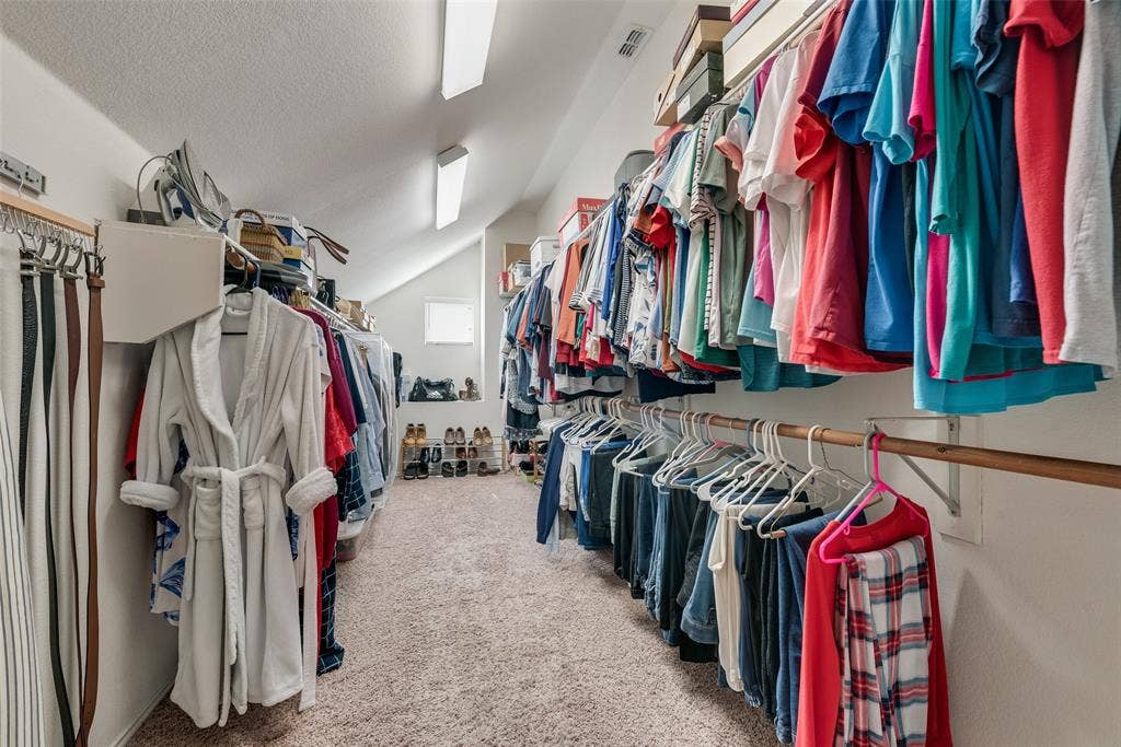 148 Oakbluff Drive, Murphy, TX 75094 Walk-in closet featuring extensive built-in hanging rods, overhead shelving, neutral carpeted flooring, and linear fluorescent lighting