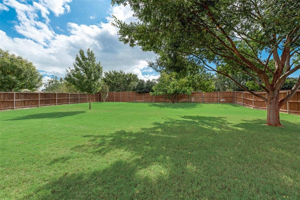 148 Oakbluff Drive, Murphy, TX 75094 Expansive backyard featuring a level lawn, mature trees, and a full-perimeter wood privacy fence