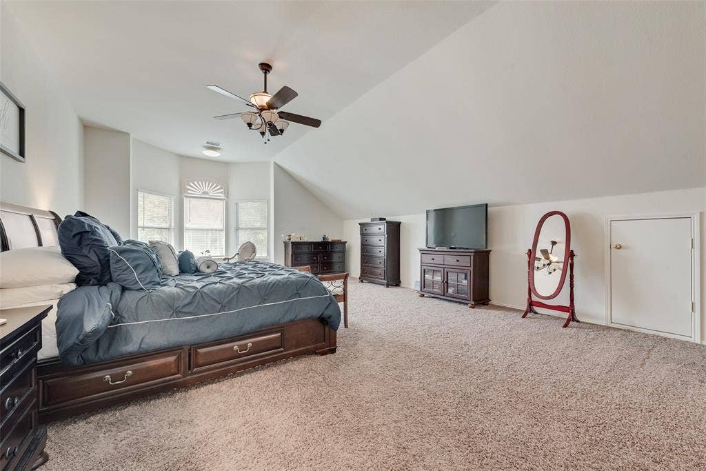 148 Oakbluff Drive, Murphy, TX 75094 Vaulted ceilings featuring a multi-pane bay window, carpeted flooring, a ceiling fan with integrated lighting, and an access door to attic storage