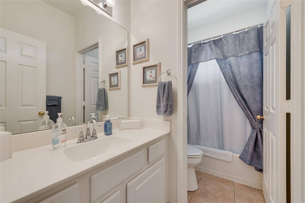 148 Oakbluff Drive, Murphy, TX 75094 Bathroom featuring a solid-surface countertop with an integrated sink, polished chrome faucet, expansive wall-to-wall mirror, built-in cabinetry, and ceramic tile flooring