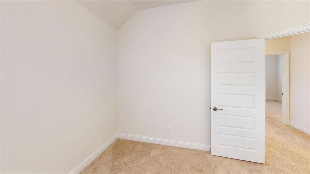 333 Elk Drive, Fate, TX 75189 Neutral-toned room featuring a vaulted ceiling, wall-to-wall carpeting, and a five-panel interior door with a brushed metallic lever handle
