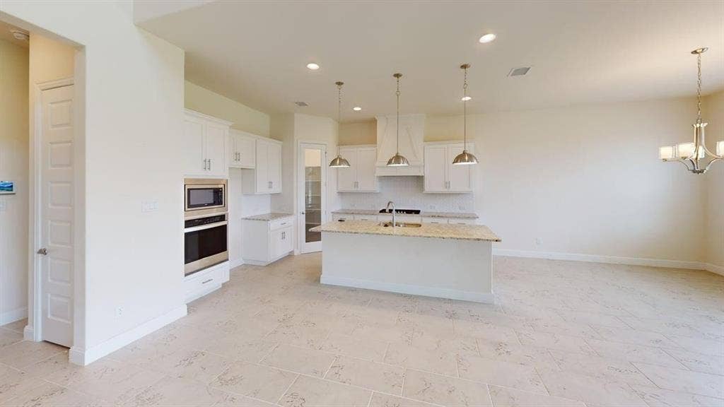 333 Elk Drive, Fate, TX 75189 Kitchen featuring white cabinetry, stone-surface countertops, built-in stainless steel double oven and microwave, stone-finish tile flooring, and three pendant lights over a central island