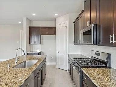 333 Elk Drive, Fate, TX 75189 Kitchen featuring dark wood cabinetry, stone countertops, stainless steel gas range, built-in microwave, and an island with a stainless steel undermount sink