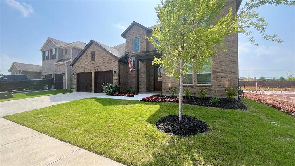 333 Elk Drive, Fate, TX 75189 Multi-story brick exterior featuring a covered entryway, dual garage bays with wood-finish doors, and landscaped front garden beds