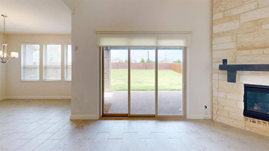 333 Elk Drive, Fate, TX 75189 High-ceilinged room featuring a floor-to-ceiling stone fireplace, wood-finish tile flooring, sliding glass door, and multi-pane windows