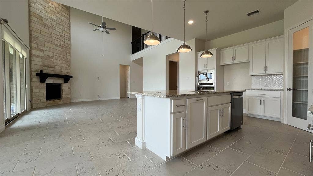 333 Elk Drive, Fate, TX 75189 Double-height ceiling with stone-faced fireplace, kitchen island featuring stone countertops, white cabinetry, herringbone-patterned tile backsplash, and tile flooring
