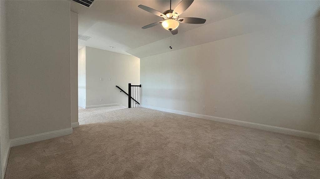 333 Elk Drive, Fate, TX 75189 Neutral-toned wall-to-wall carpeting, vaulted ceiling with a central brushed-nickel ceiling fan, and a staircase featuring a black metal balustrade