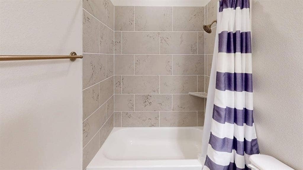 333 Elk Drive, Fate, TX 75189 Full-height shower surround featuring large-format neutral tile with decorative inlay, integrated corner shelf, and metallic finish shower head and wall-mounted towel bar