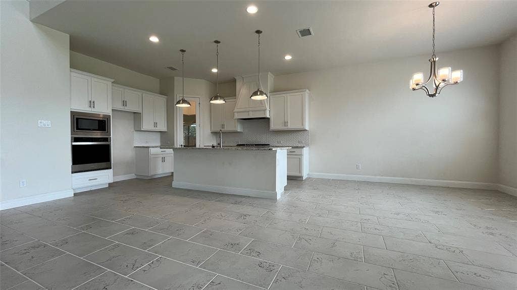 333 Elk Drive, Fate, TX 75189 Kitchen featuring white cabinetry, an expansive center island, integrated stainless steel double wall ovens, three brushed metal pendant lights, and large-format tile flooring