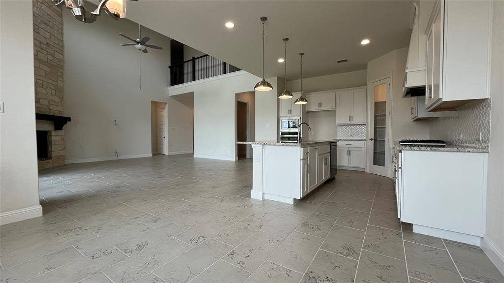 333 Elk Drive, Fate, TX 75189 High-ceilinged interior featuring a floor-to-ceiling stone fireplace, large kitchen island with integrated sink, shaker-style cabinetry, patterned tile flooring, and recessed pendant lighting
