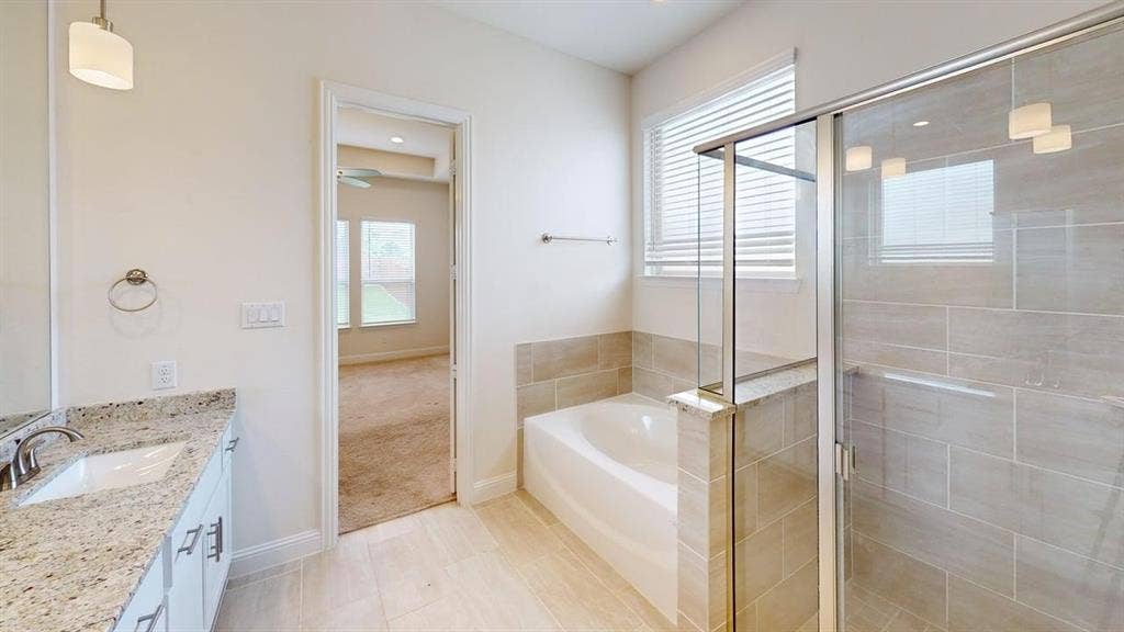333 Elk Drive, Fate, TX 75189 Bathroom featuring a stone countertop vanity, a deep soaking tub with tile surround, a glass-enclosed shower, and large-format tile flooring