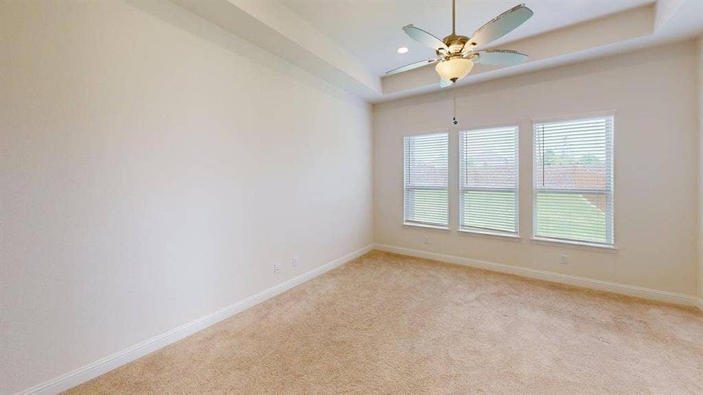 333 Elk Drive, Fate, TX 75189 Room featuring a tray ceiling, neutral wall-to-wall carpeting, three windows with horizontal blinds, and a central ceiling fan with an integrated light fixture