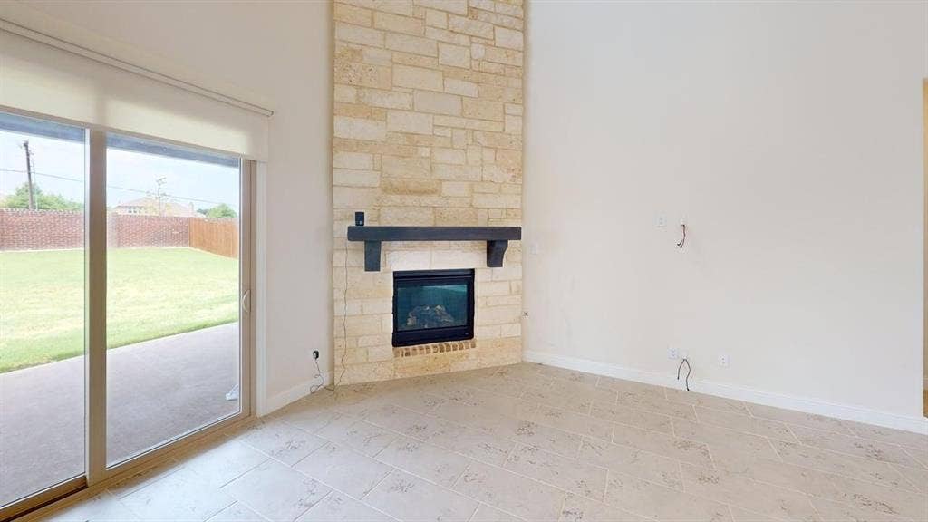 333 Elk Drive, Fate, TX 75189 Floor-to-ceiling stone fireplace with a dark wood mantel, sliding glass door, and tile flooring