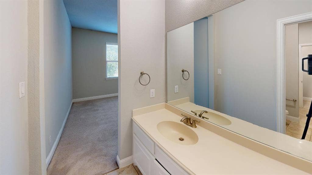7005 Golf Club Drive, McKinney, TX 75070 Vanity featuring a solid-surface integrated sink, white cabinetry, metallic faucet hardware, and a large wall-mounted mirror