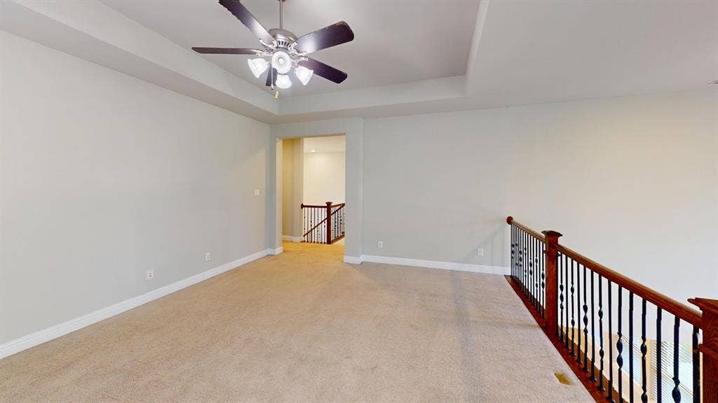 7005 Golf Club Drive, McKinney, TX 75070 Tray ceiling featuring a central multi-blade ceiling fan with integrated lighting and a decorative balustrade with wood handrails and black metal spindles
