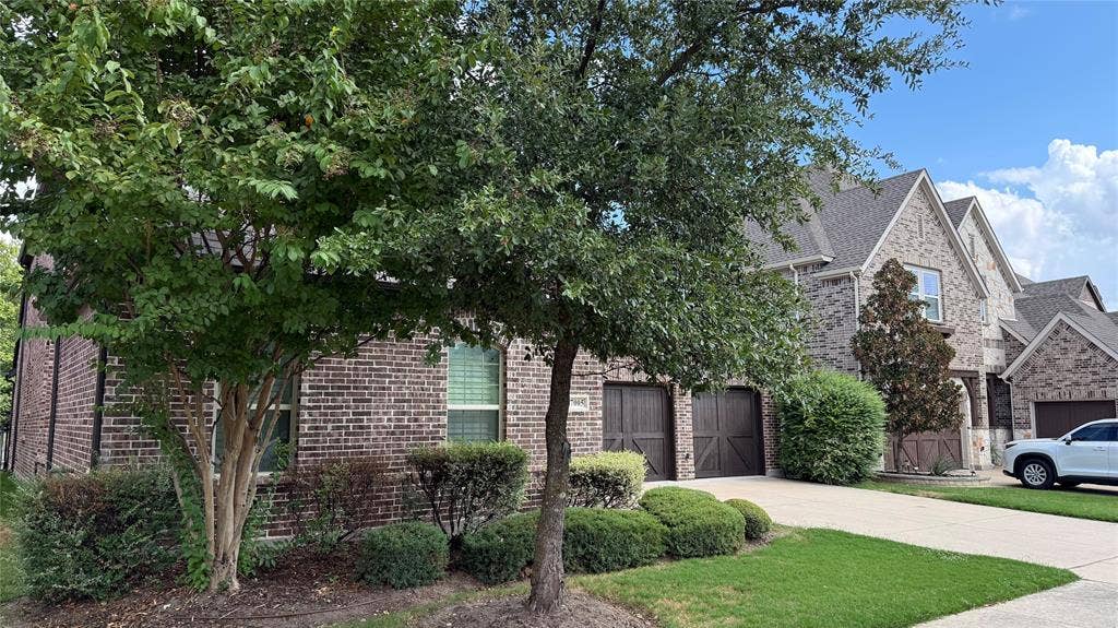 7005 Golf Club Drive, McKinney, TX 75070 Multi-level brick exterior featuring a steeply pitched roofline, wood-finish garage doors, and a concrete driveway