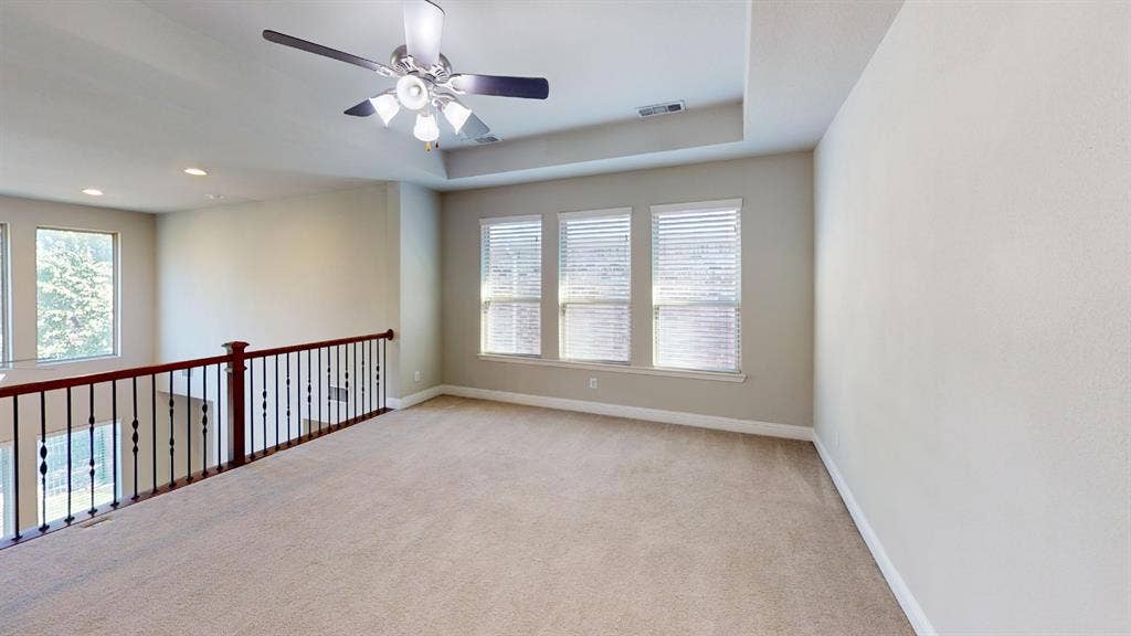 7005 Golf Club Drive, McKinney, TX 75070 Tray ceiling featuring a central multi-light ceiling fan, neutral carpeting, and a wooden handrail with metal balusters