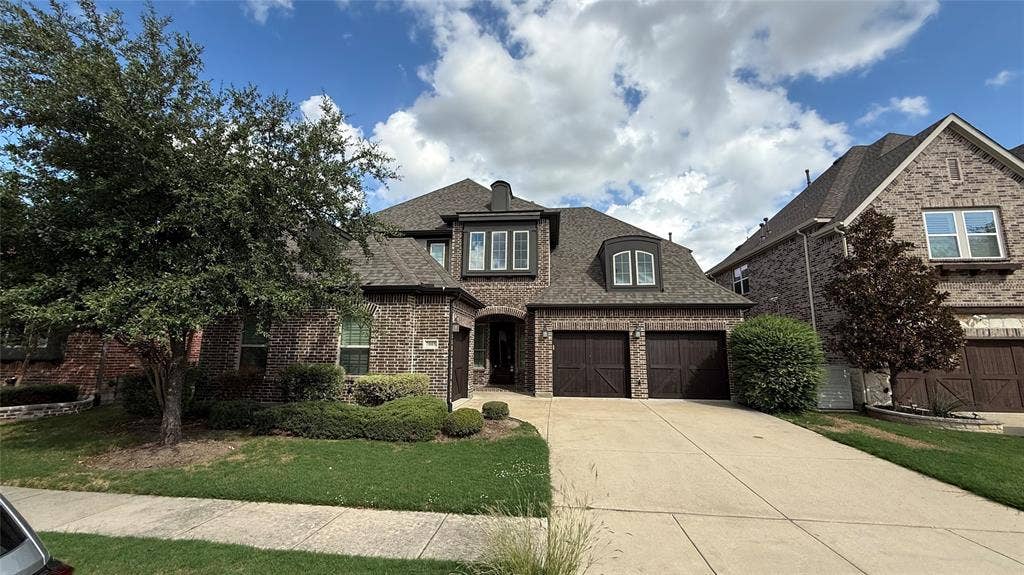 7005 Golf Club Drive, McKinney, TX 75070 Two-story brick exterior featuring a multi-gabled roofline, dormer window, integrated two-car garage with carriage-style doors, and manicured landscaping