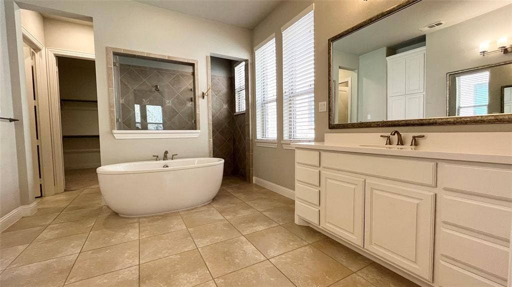 7005 Golf Club Drive, McKinney, TX 75070 Freestanding soaking tub, vanity with solid surface countertop, large framed wall mirror, tile flooring, and walk-in shower with tiled surround