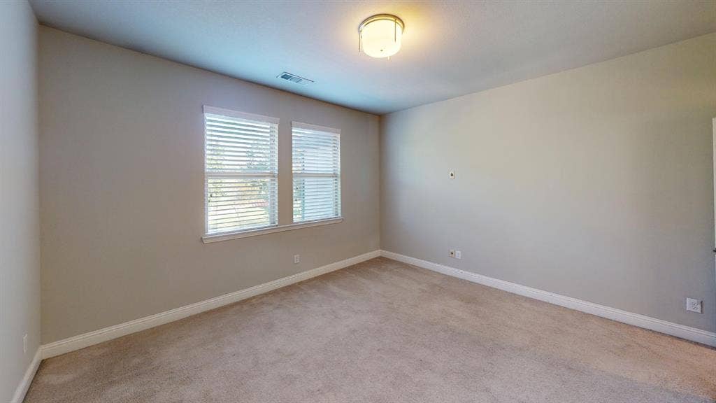 7005 Golf Club Drive, McKinney, TX 75070 Neutral-toned interior space featuring light-colored wall-to-wall carpeting, dual windows with horizontal blinds, and a circular flush-mount ceiling light fixture
