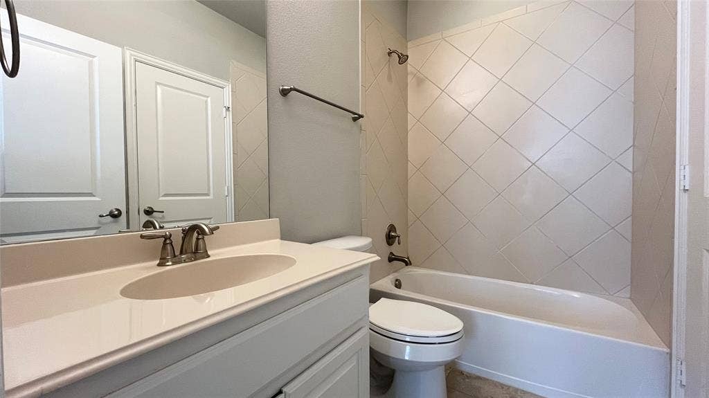 7005 Golf Club Drive, McKinney, TX 75070 Bathroom featuring a vanity with an integrated basin, countertop-mounted metal faucet, diagonal tile wall surround, and combination tub-shower with metal fixture
