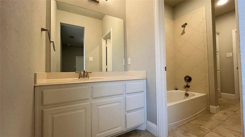 7005 Golf Club Drive, McKinney, TX 75070 Bathroom featuring a white vanity cabinet with an integrated countertop, large wall-mounted mirror, and tub-shower combination with diagonal tile surround