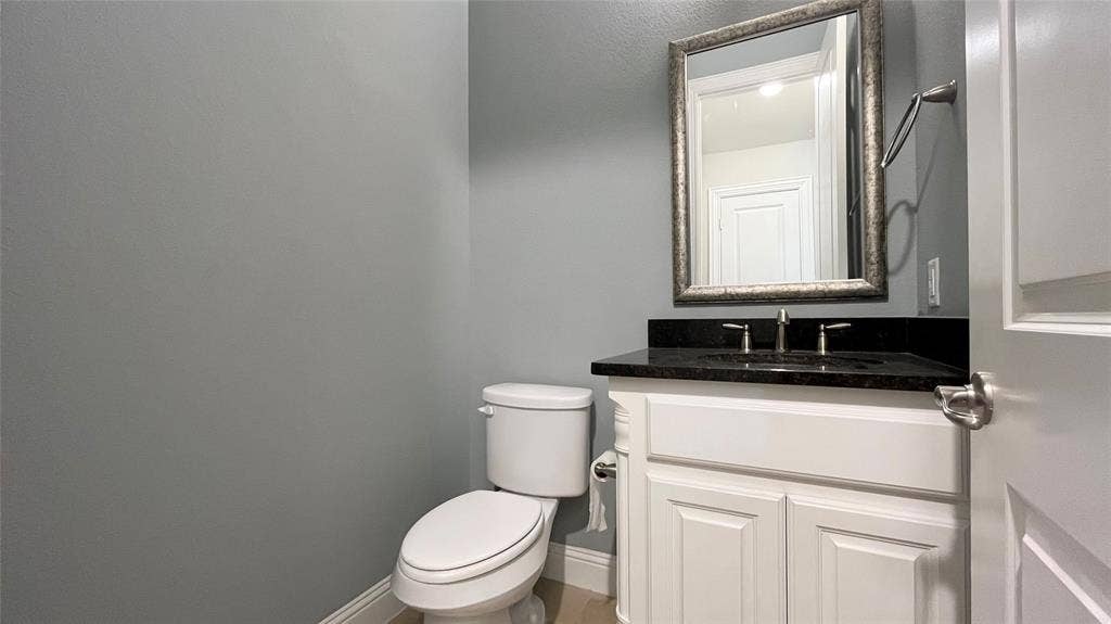 7005 Golf Club Drive, McKinney, TX 75070 White cabinetry vanity with a dark stone countertop, integrated sink, wall-mounted mirror, and chrome hardware