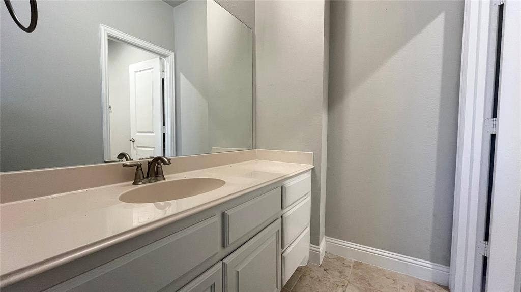 7005 Golf Club Drive, McKinney, TX 75070 Vanity featuring light-toned cabinetry, an integrated oval sink, stone-finish countertop, polished metal faucet, and wall-to-wall mirror with stone-finish tile flooring