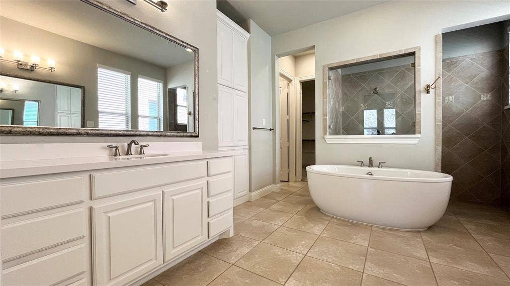 7005 Golf Club Drive, McKinney, TX 75070 Bathroom featuring a double-sink vanity with white cabinetry, quartz countertop, freestanding soaking tub, and tile flooring