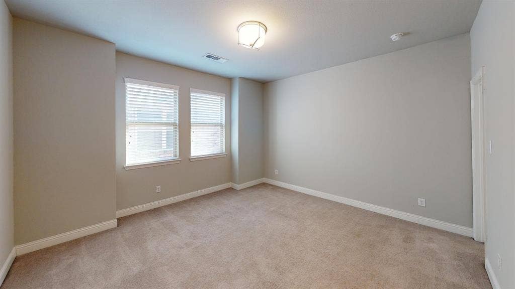 7005 Golf Club Drive, McKinney, TX 75070 Neutral-toned interior space featuring neutral wall paint, wall-to-wall carpeting, dual windows with horizontal blinds, and a central ceiling-mounted light fixture