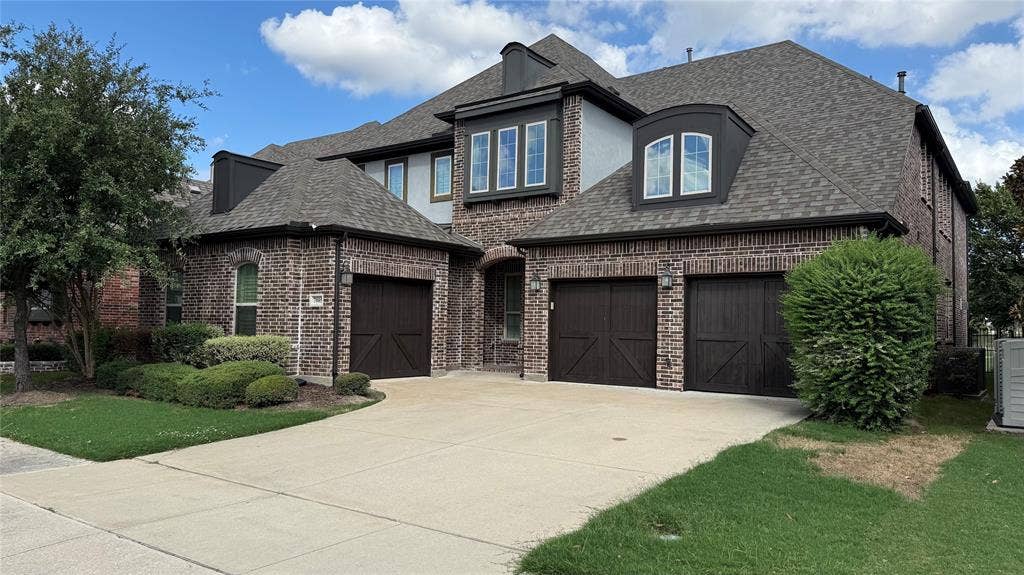 7005 Golf Club Drive, McKinney, TX 75070 Multi-level exterior featuring a brick facade, multi-gabled roofline, three-car garage with carriage-style doors, and decorative arched window dormers