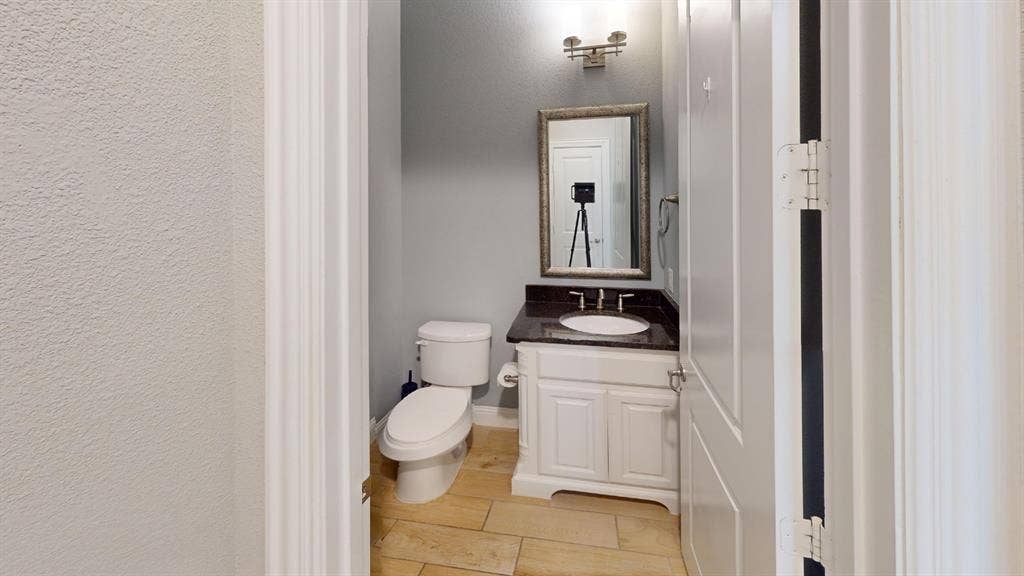 7005 Golf Club Drive, McKinney, TX 75070 White vanity cabinet featuring a dark stone countertop, undermount oval sink, stone-finish flooring, and wall-mounted vanity lighting