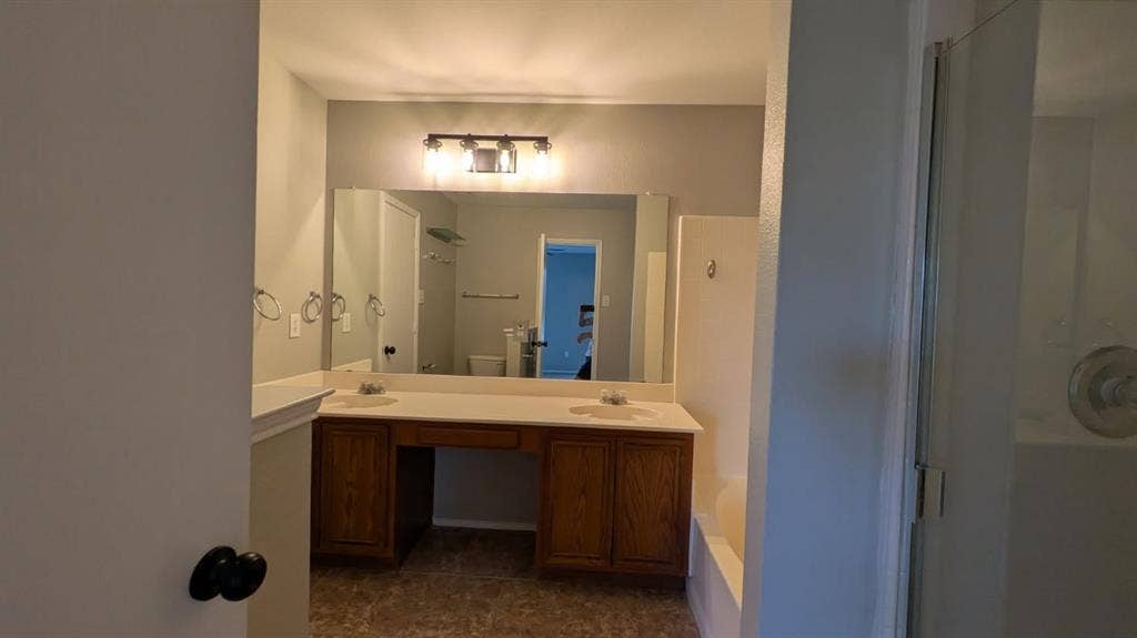 408 Oxford Loop Loop, Princeton, TX 75407 Double vanity with inset sinks, wood-finish cabinetry, full-width vanity mirror, tri-light fixture, and tiled shower enclosure