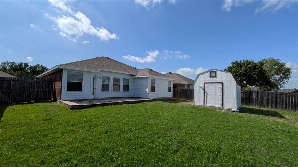 408 Oxford Loop Loop, Princeton, TX 75407 Rear exterior featuring a concrete patio, white horizontal siding, a pitched shingle roof, and a detached storage shed set within a fenced yard