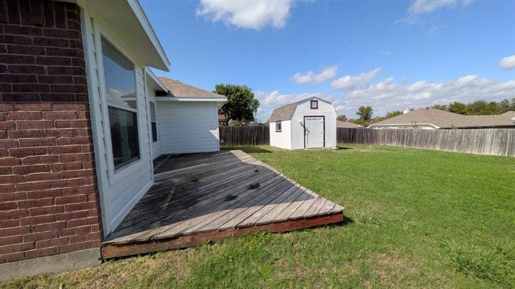408 Oxford Loop Loop, Princeton, TX 75407 Rear exterior featuring a wood deck, lawn, detached storage structure, and perimeter fencing