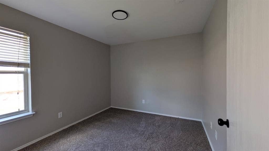 408 Oxford Loop Loop, Princeton, TX 75407 Neutral-toned interior space featuring neutral wall paint, wall-to-wall carpeting, a window with horizontal blinds, and a circular flush-mount ceiling light fixture