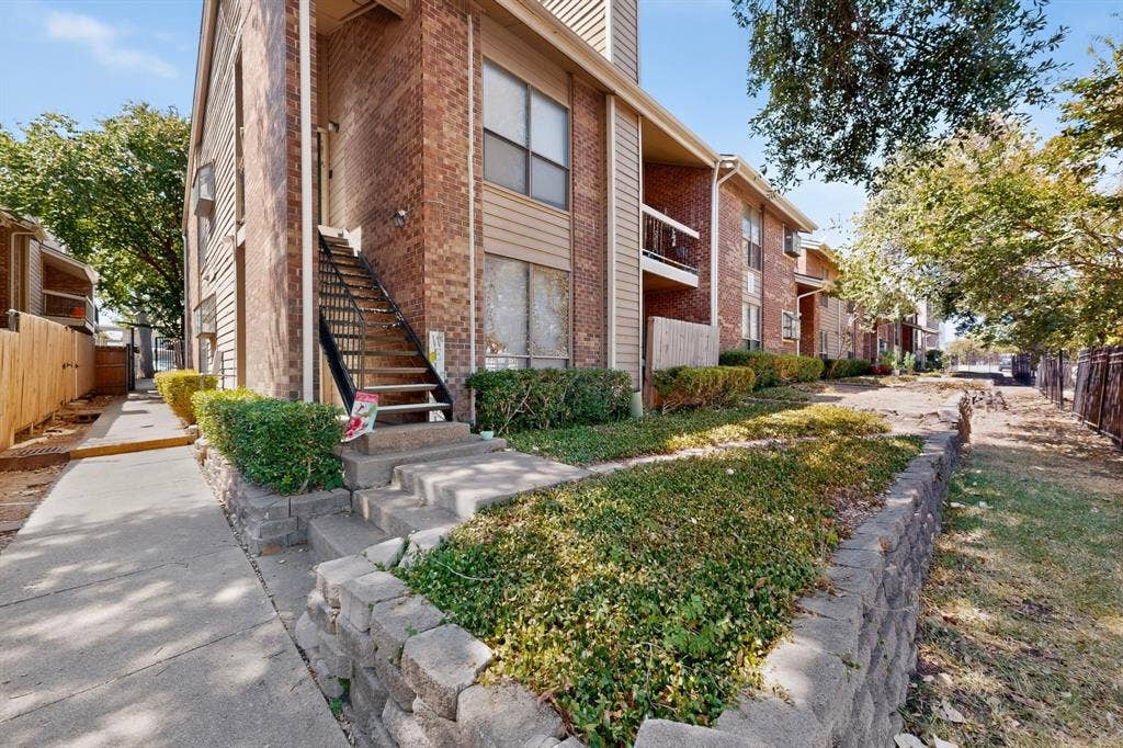 5750 Phoenix Drive, #6, Dallas, TX 75231 Brick exterior with vertical siding accents, concrete walkways, mature trees, and a metal staircase with railing