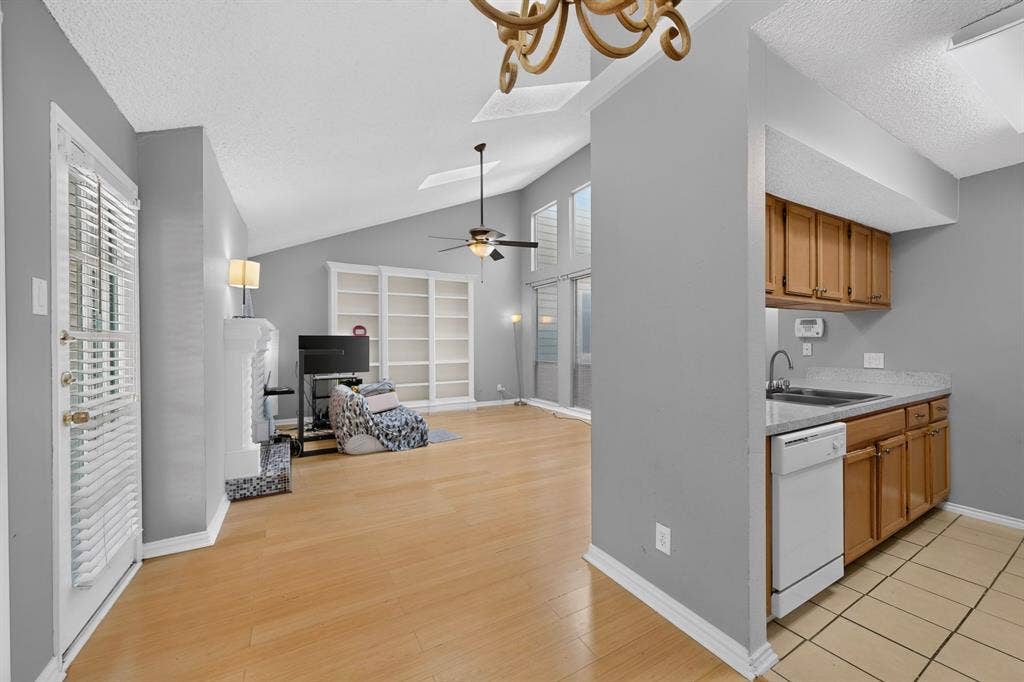 5750 Phoenix Drive, #6, Dallas, TX 75231 Living area with vaulted ceiling, wood-finish flooring, built-in shelving, fireplace, and integrated kitchen with wood cabinetry